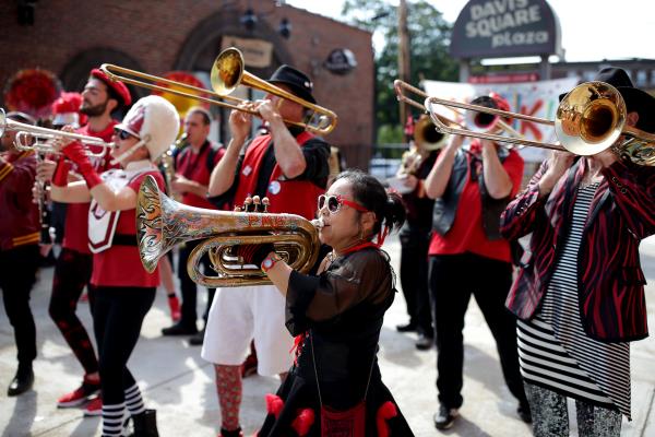 Musicians in unmatched red, white and black outfits march playing brass instruments.