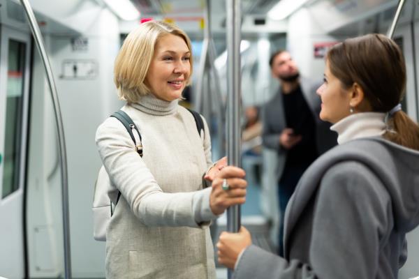 two women standing on a subway car smiling at each other