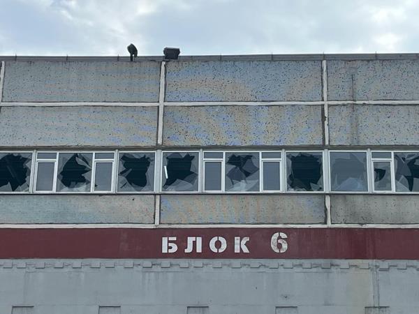 The grey facade of a building shows a line of broken windows.